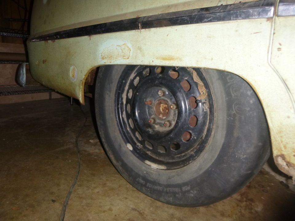 Close-up of a flat rear tire and rusty quarter panel on a light green vintage vehicle.