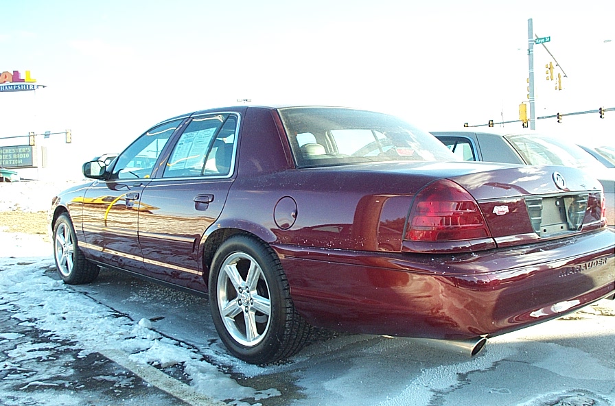 Maroon Ford Crown Victoria parked on a snowy lot, rear view. Another car is parked next to it