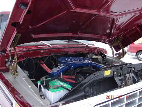 1979 Ford F-150 - The open hood of a dark red 1979 Ford F-150 reveals its engine bay. The V8 engine features a blue air cleaner assembly and red spark plug w…