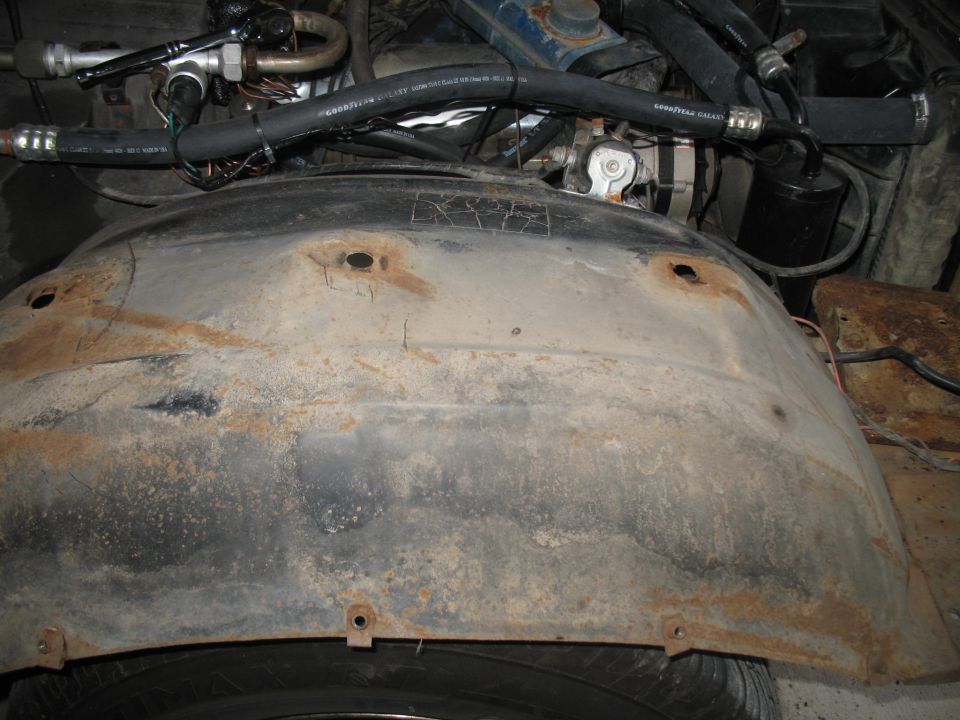 Rusty inner fender well with hoses and engine parts above.