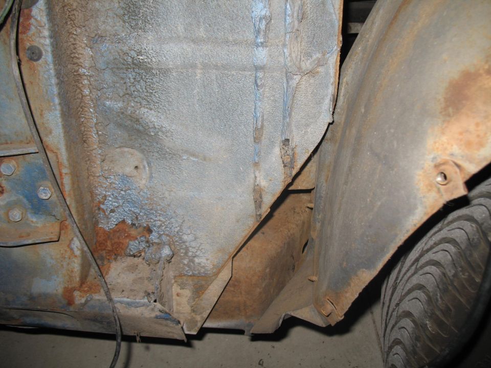 Underside of a vehicle showing heavy rust and peeling blue paint.