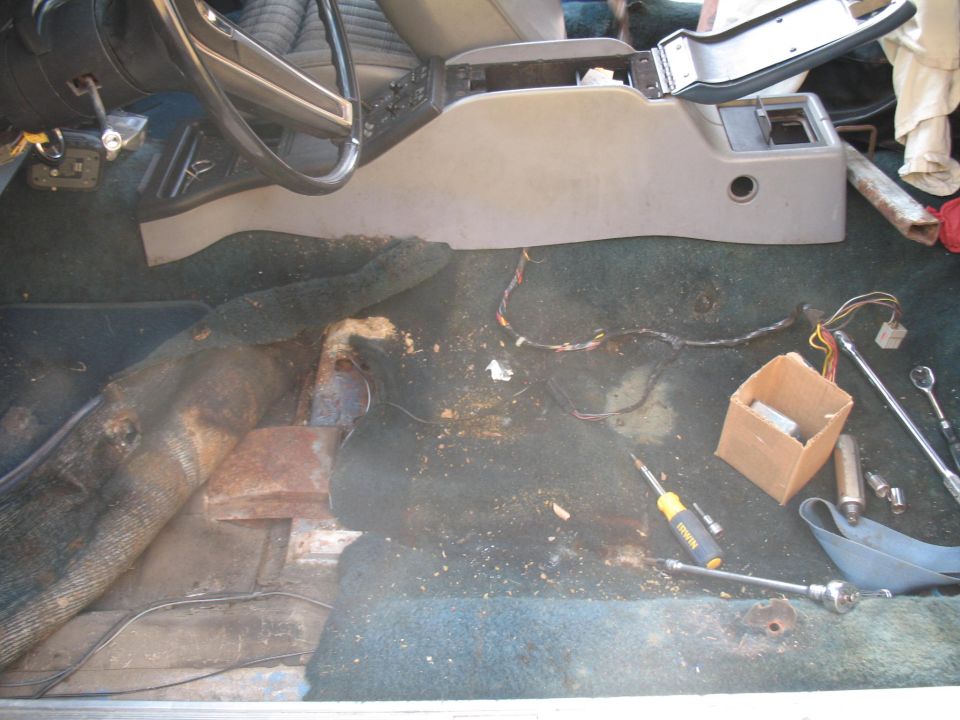 Interior of a vehicle with center console removed, showing wiring and tools on the floor.