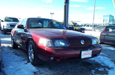 2001 Ford Crown Victoria - A red sedan with a vertical grille and chrome wheels is parked in a lot with snow on the ground.