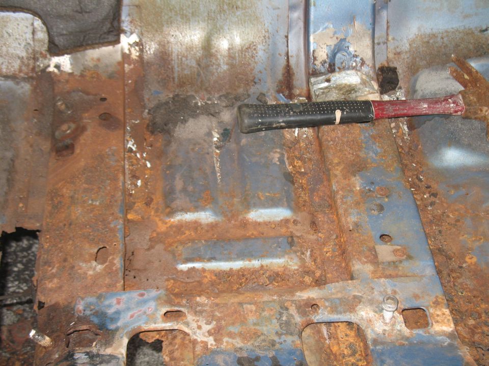 rusted out floor pan with a hammer resting on it