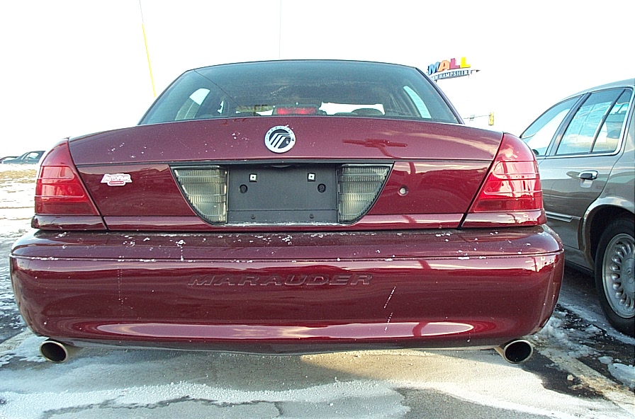 Rear of a red Mercury Marauder with dual exhaust. Another car is parked to its right