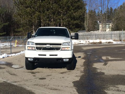2006 Chevrolet Silverado 2500 - A white Chevrolet Silverado 2500 pickup truck is parked in an asphalt lot with some snow on the ground. The truck is viewed from the front…