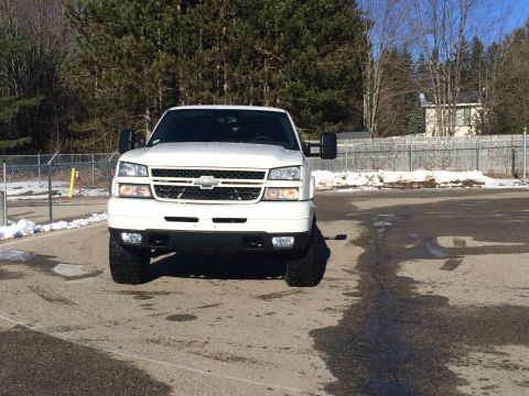 2006 Chevrolet Silverado 2500 - The front view of a white Chevrolet Silverado 2500 pickup truck is shown parked on an asphalt surface with patches of snow and ice visible.…