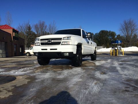 2006 Chevrolet Silverado 2500 - A white Chevrolet Silverado 2500 pickup truck is parked on a wet, icy surface in front of a car wash and gas station on a clear, sunny day.