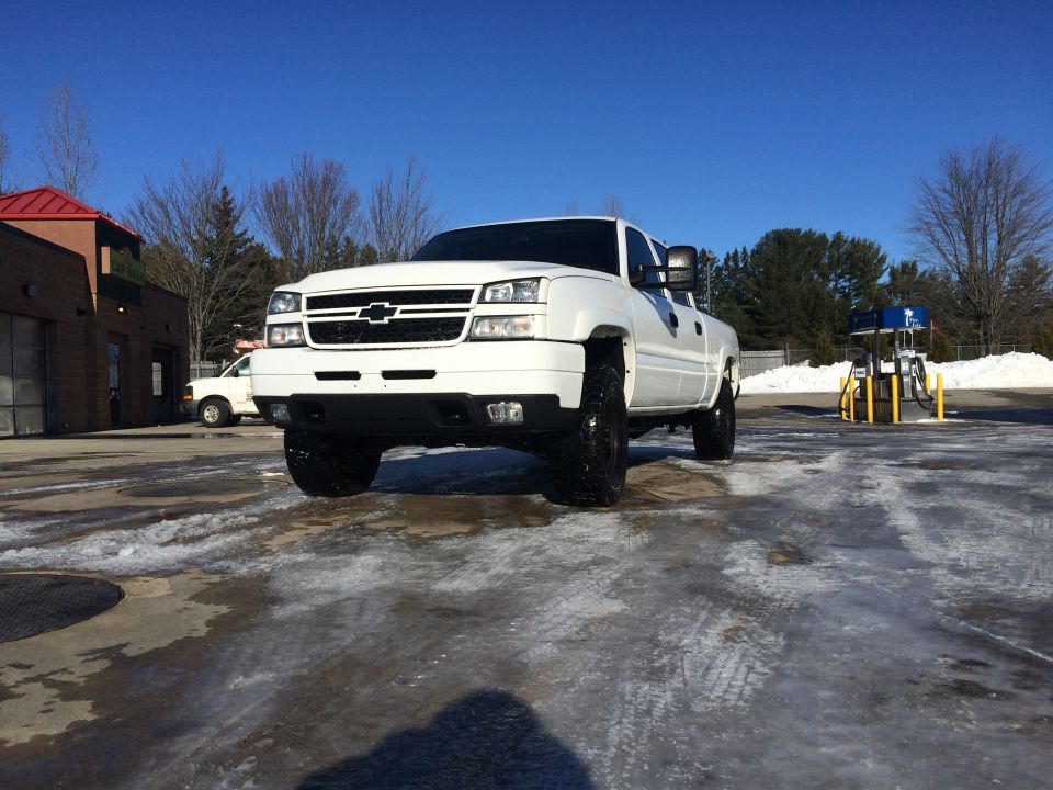 White Chevrolet Silverado 2500 pickup truck parked on icy ground near a car wash and gas station.