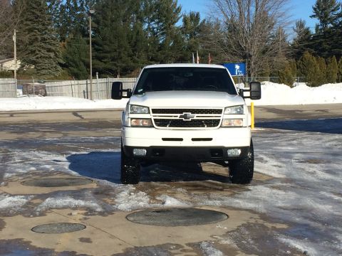 2006 Chevrolet Silverado 2500 - A white Chevrolet Silverado 2500 pickup truck is parked on a wet, icy surface with snow in the background. The truck is viewed from the fro…