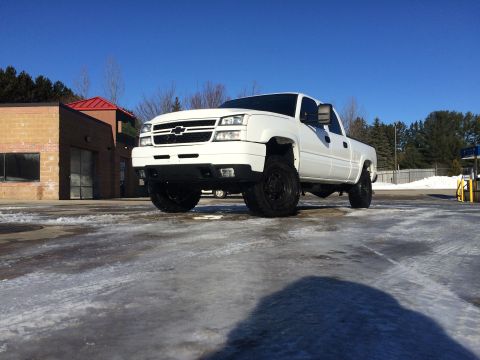 2006 Chevrolet Silverado 2500 - A white Chevrolet Silverado 2500 pickup truck is parked on a wet, icy surface in front of a car wash on a clear, sunny day. The truck is li…