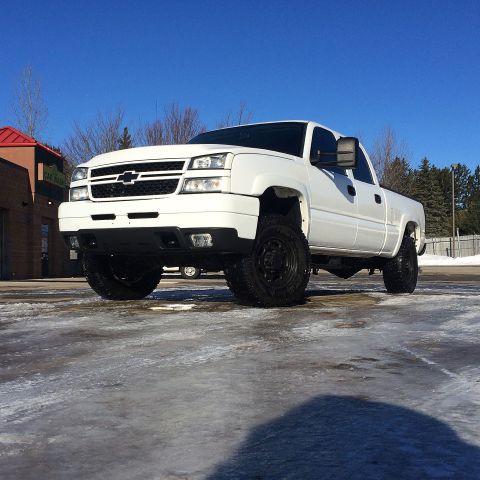 2006 Chevrolet Silverado 2500 - A white Chevrolet Silverado 2500 pickup truck is parked on a wet, icy surface with a car wash in the background. The truck is seen from a l…