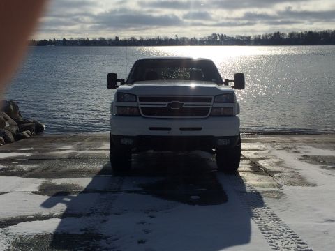 2006 Chevrolet Silverado 2500 - A white Chevrolet pickup truck is parked on a boat ramp facing the water. The sun reflects off the water and the truck's grille.