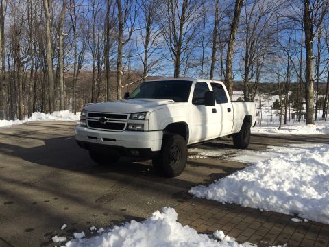 2006 Chevrolet Silverado 2500 - A white Chevrolet Silverado 2500 pickup truck is parked on an asphalt driveway with snow on the ground and trees in the background.