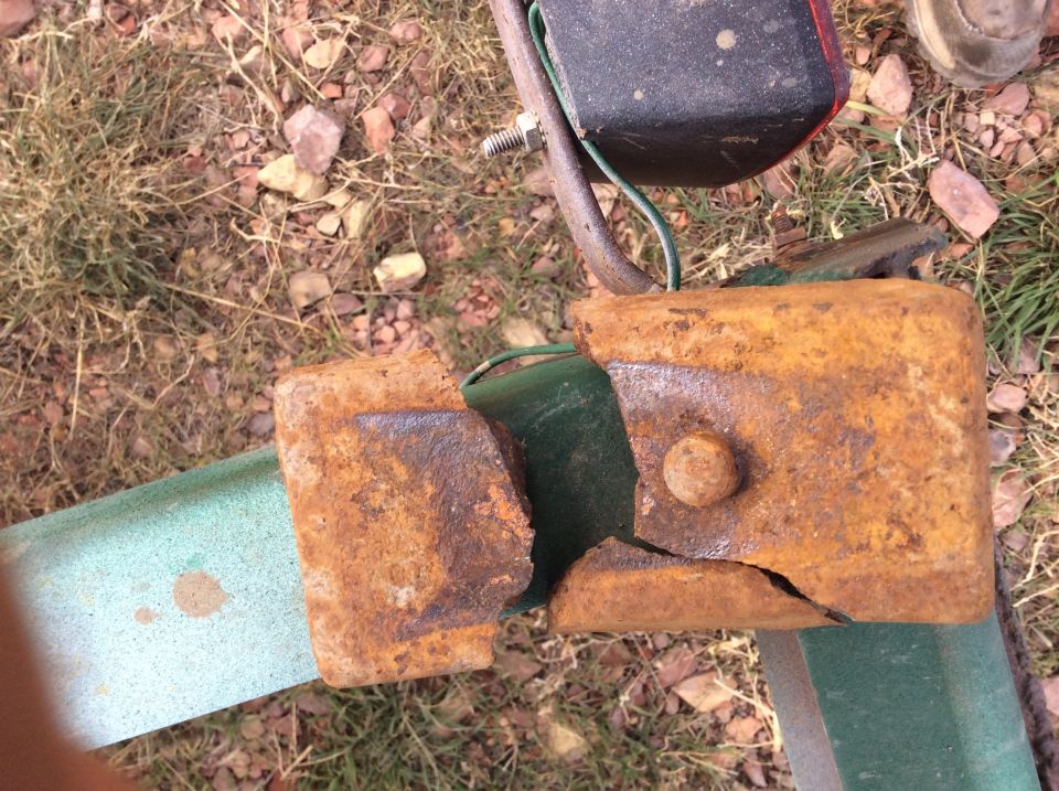 Rusted, cracked jack/coupler bracket on green trailer frame with wiring and taillight, gravel ground