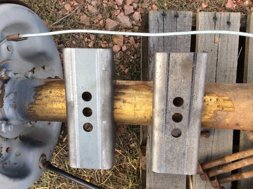 Rusty axle tube with brake drum and two three-hole metal bracket sleeves on a wooden pallet