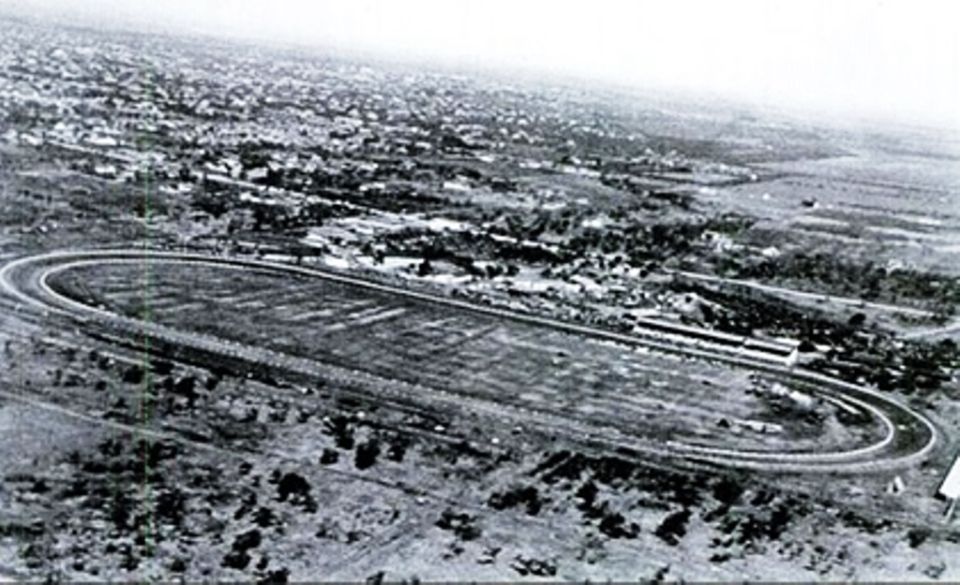 Aerial view of a horse racing track with grandstands and a town in the background