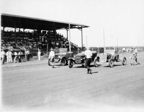 1909 Ford Model T - Cars and people gather near a grandstand at a race event.