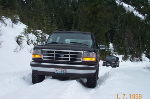 1995 Ford Bronco - A 1995 Ford Bronco navigates a snow-covered road, with a second vehicle following in the distance.