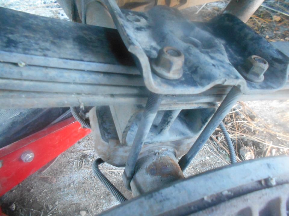Rear leaf spring suspension with U-bolts and mounting bracket. A red jack is visible to the left