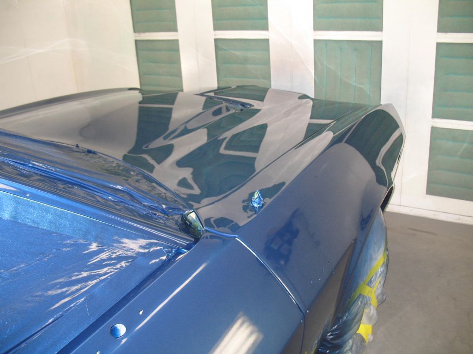 Blue car hood with scoop and fender in a paint booth. Yellow tape on fender