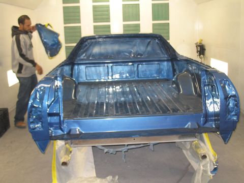1972 Ford Ranchero - A man stands in a paint booth next to a freshly painted blue pickup truck bed.