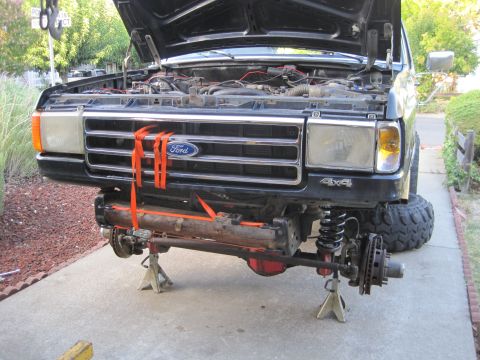 1989 Ford Bronco - Front end of a black Ford truck undergoing repairs, with the axle detached and the hood open.