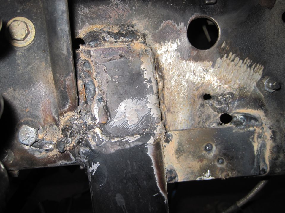 Close-up of a vehicle frame with significant welding repairs and some rust