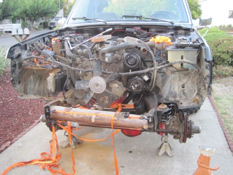 1989 Ford Bronco - The front end of a 1989 Ford Bronco is disassembled, showing the engine and suspension components supported by jack stands.