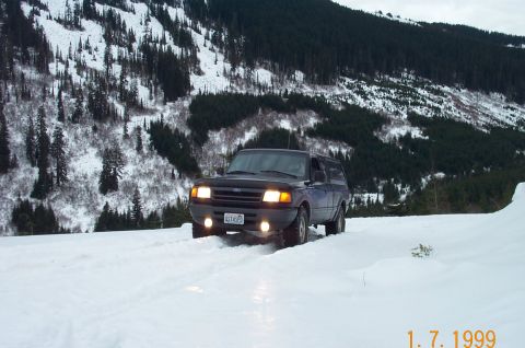 1995 Ford Bronco - A 1995 Ford Bronco navigates a snow-covered mountain road, its headlights cutting through the winter landscape.