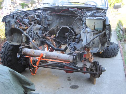 1989 Ford Bronco - 1989 Ford Bronco chassis undergoing work, engine bay is open and suspension is exposed.