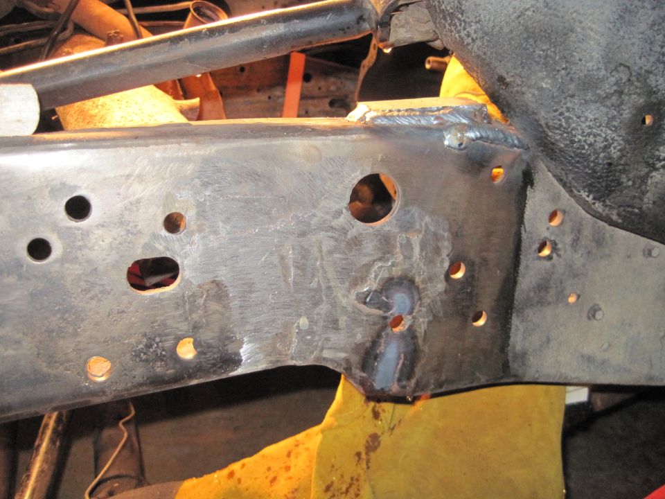 Close-up of a rusty metal frame rail with several holes and fresh welds