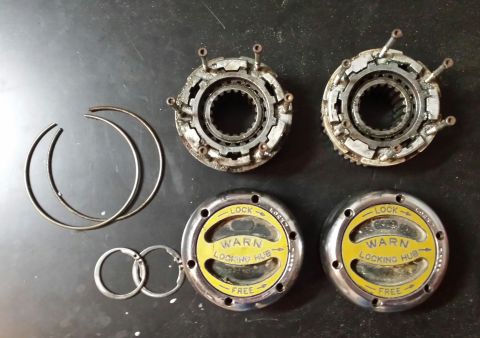 1995 Ford Bronco - Two WARN locking hubs and associated internal components are laid out on a dark surface.