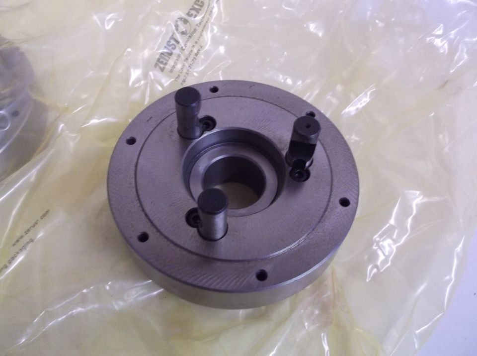 Metal lathe chuck with three jaws, wrapped in plastic packaging