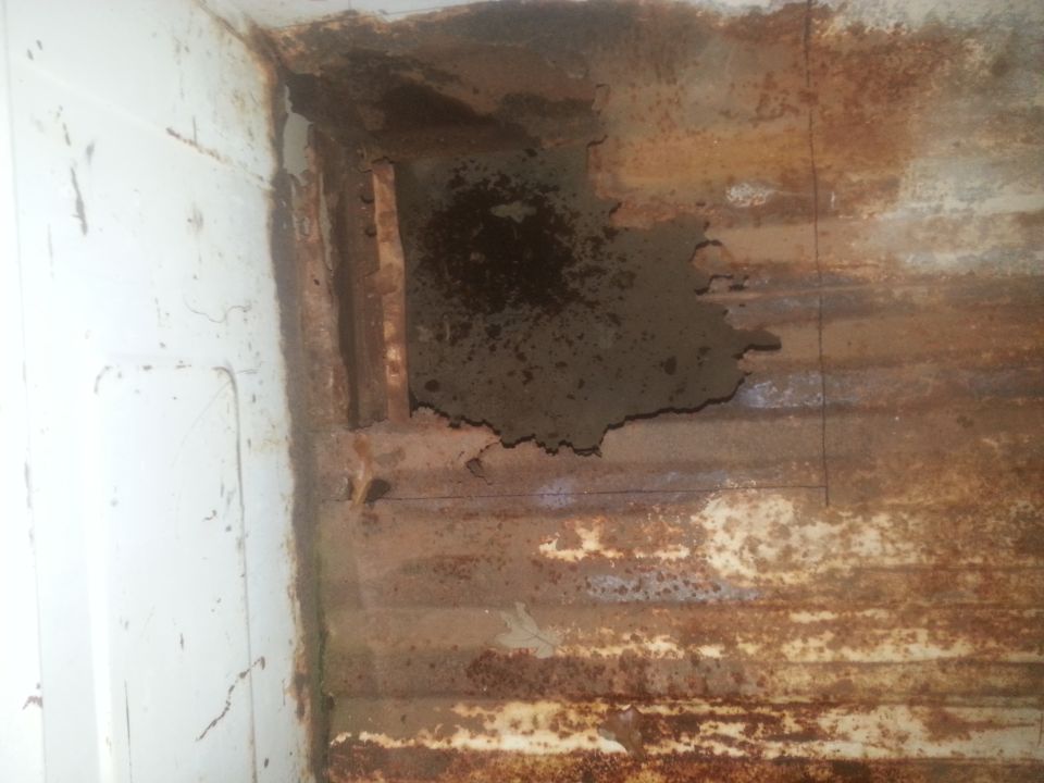 Rusted truck bed with large hole showing structural damage and white painted interior wall