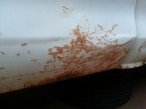 1973 Ford F-100 - Rust spots are visible on the side of a white truck fender, indicating wear and tear.