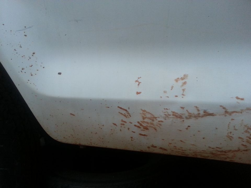 Close-up of a white vehicle's lower body panel with dirt and mud splatters