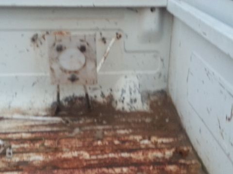 1973 Ford F-100 - The interior of a white truck bed shows significant rust on the floor and a mounting bracket.