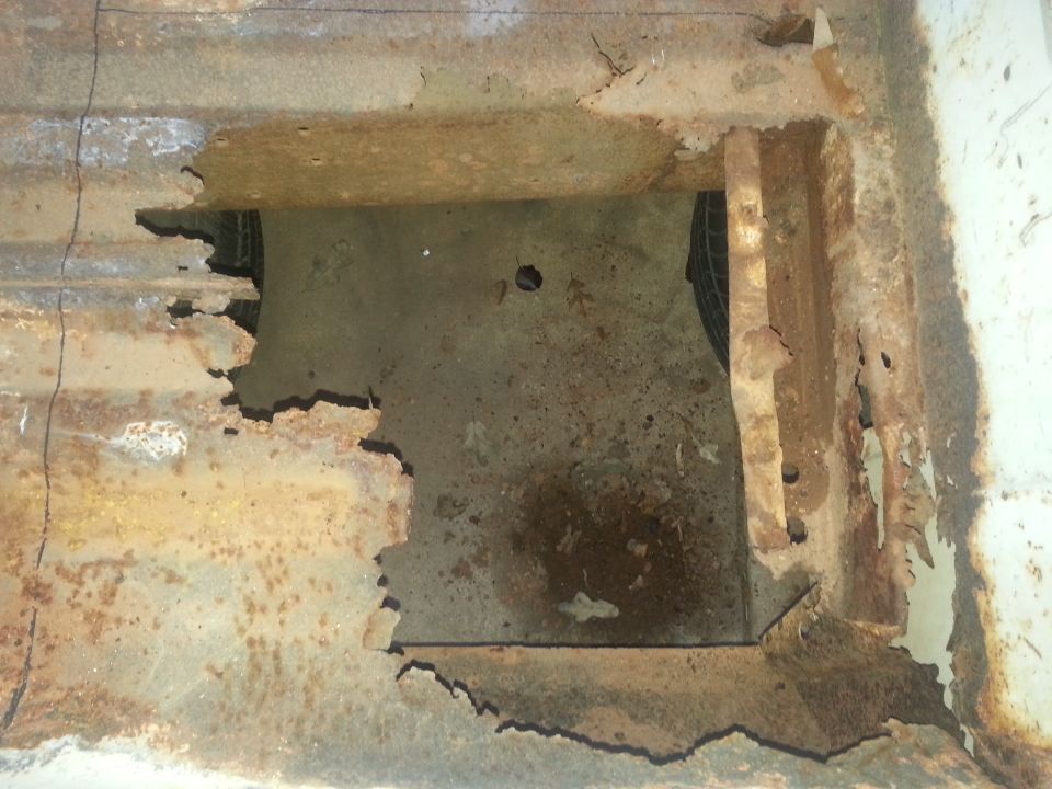 Severely rusted truck bed floor with a hole revealing a tire