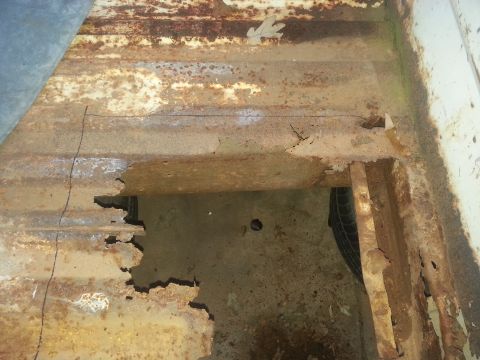 1973 Ford F-100 - Severe rust damage on the bed floor of a truck, revealing the frame and a spare tire below.
