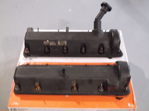 1995 Mercury Grand Marquis - Two black valve covers are shown, one with a spark plug wire boot attached, resting on a box.