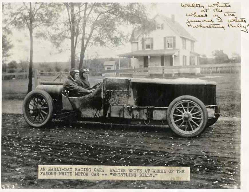 Racing car with two occupants, side view. Dark body, spoked wheels