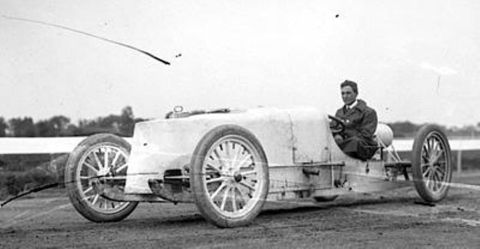 1909 Ford Model T - Driver sits in a vintage race car with a tall, boxy radiator shroud and spoked wheels.
