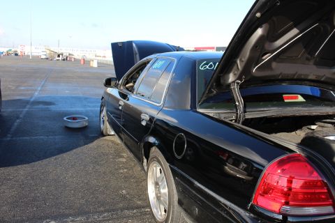 2003 Ford Crown Victoria - Rear quarter of a black sedan at a track with trunk and hood open, a tech number marked on the side glass and red taillights.