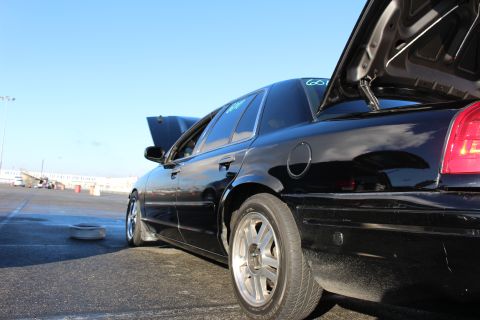 2003 Ford Crown Victoria - Low rear three-quarter view of a black sedan with chrome wheels and an open trunk, parked on a sunlit drag strip.