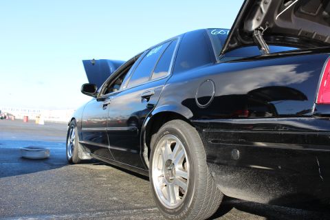 2003 Ford Crown Victoria - Low side-rear view of a black sedan with chrome wheels, open doors and raised trunk on track pavement.