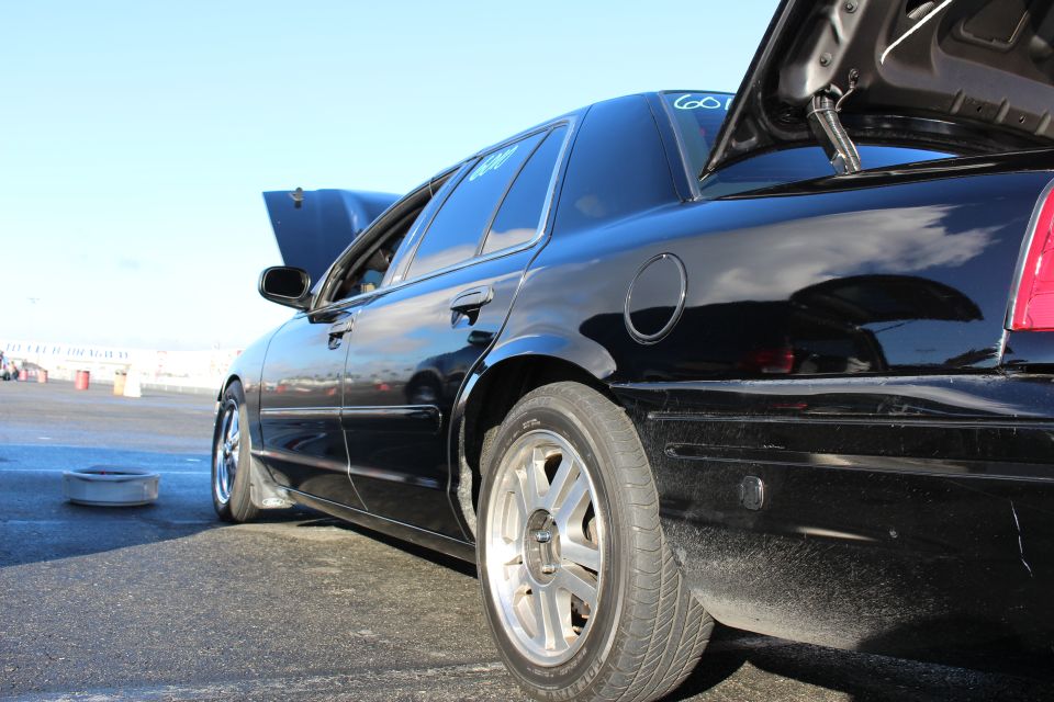 Low side rear view of a black sedan with open doors and trunk on track pavement