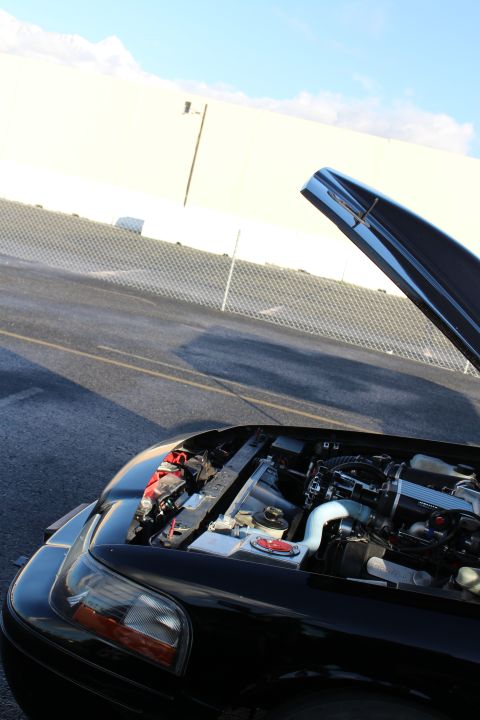 2003 Ford Crown Victoria - front corner of a black car with the hood raised, exposing an engine bay with intake piping, parked at a drag strip.