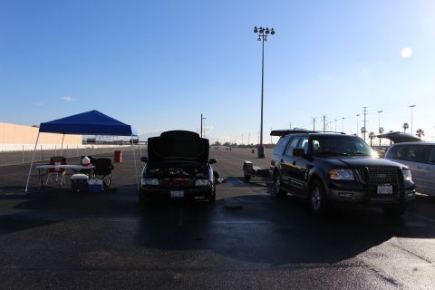 2003 Ford Crown Victoria - wide lot scene with a black sedan, a black Ford Expedition, a blue canopy and a tall stadium light pole under blue sky.