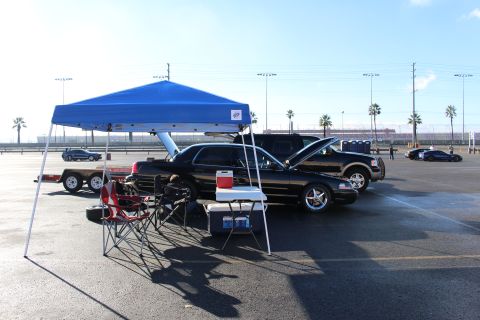 2003 Ford Crown Victoria - black sedan parked under a blue pop-up canopy with folding chairs and a table in a large open asphalt lot.